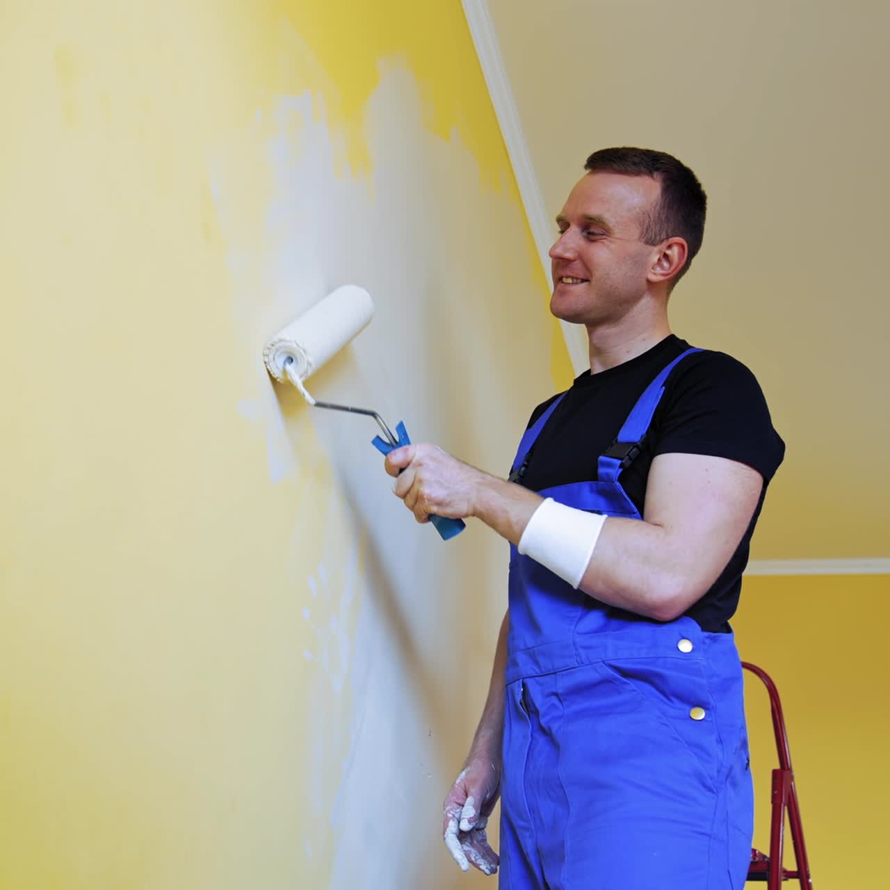Painter with a paint roller in action. Happy young adult man painting the wall of the room in a flat. Interior decoration