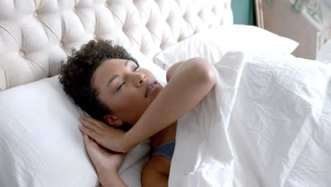 Biracial-woman-sleeping-in-bed-in-bedroom,-slow-motion