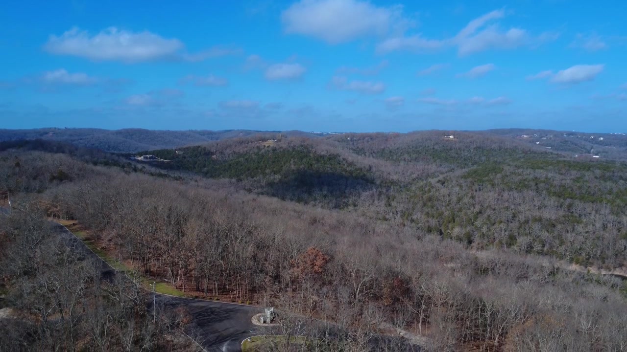 Lag på lag af skovklædte bjergrygge strækker sig over Missouri Ozarks, mens dronen svæver over en stille dal nær Branson West. Scenen fanger den enorme skala og tidløse skønhed.