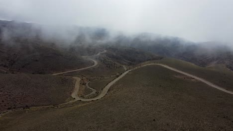 Car-drives-dirt-road-winding-through-foggy-rolling-hills-in-Argentina