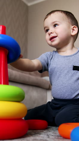 joyful baby boy playing with toy pyramid. kid takes two toy rings and bangs them together. low angle view. vertical video