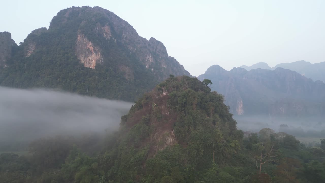tomada de un avión no tripulado de la niebla que se eleva sobre acantilados dentados en vang vieng, la capital de la aventura de laos