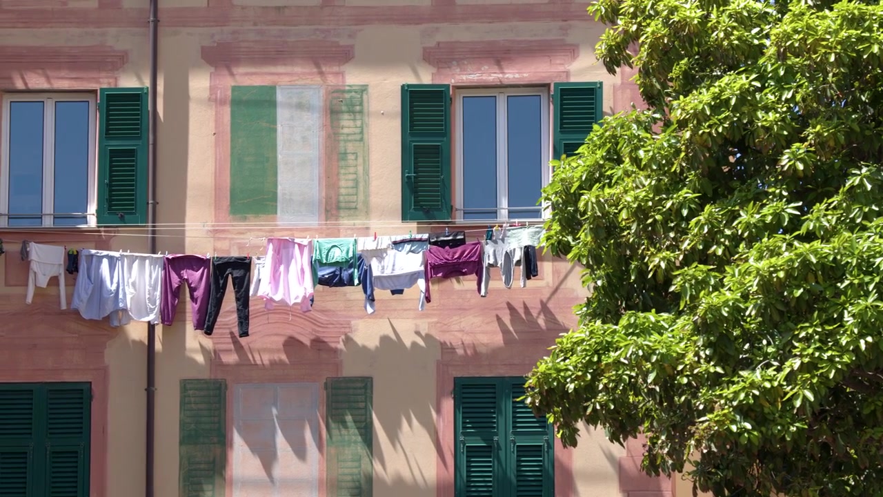 Bucato colorato si asciuga su uno stendibiancheria contro una facciata rosa con persiane verdi in Italia.