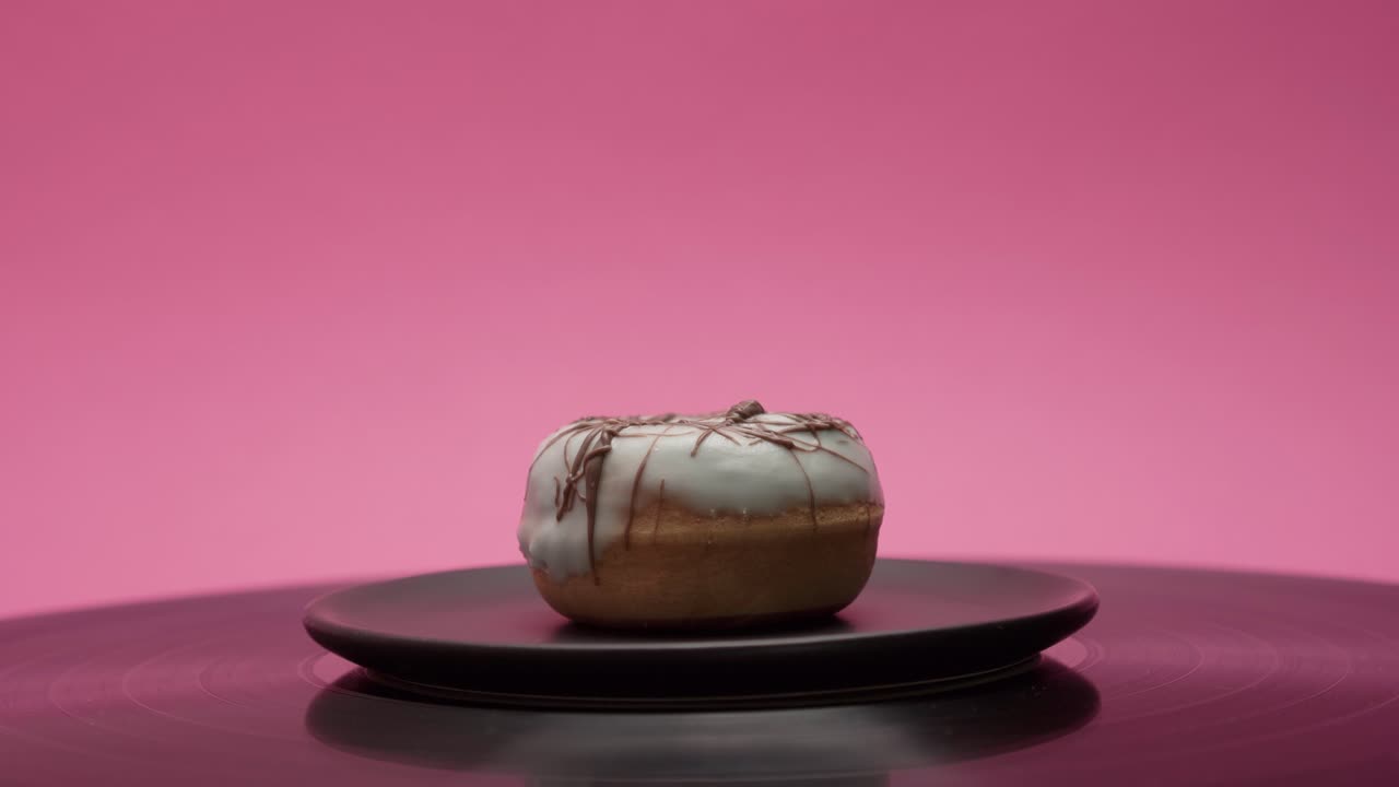 Delicious American donut with blue and black chocolate is turning in a circle on a pink background