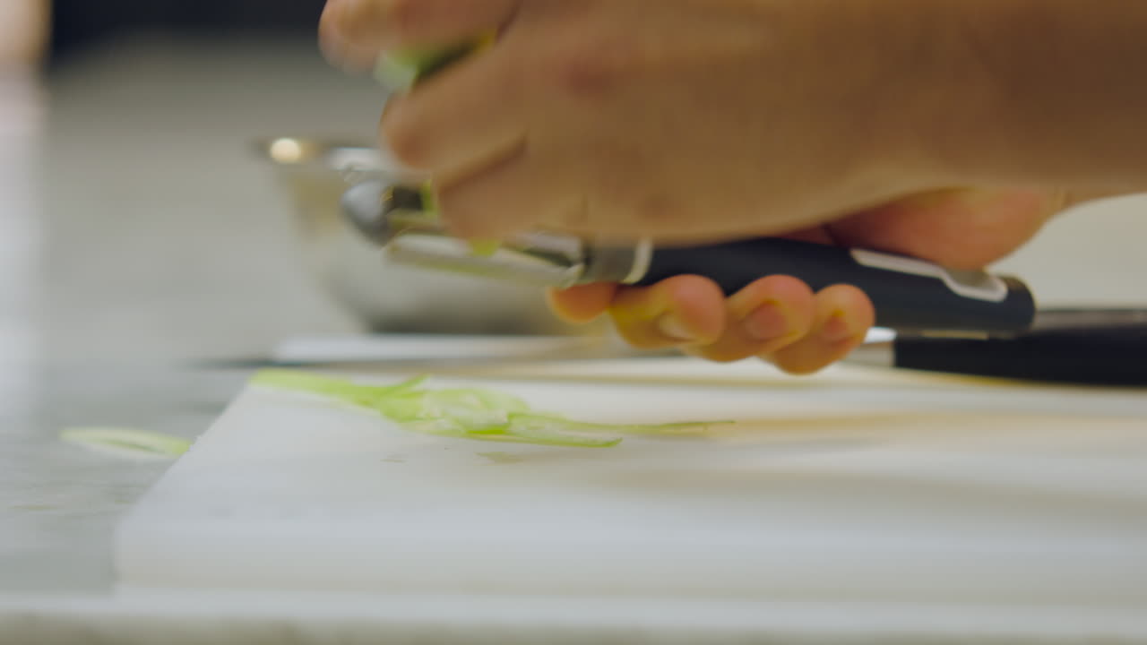 Close-up of a chef's hands peeling a green apple with a peeler on a chopping board on a white counter