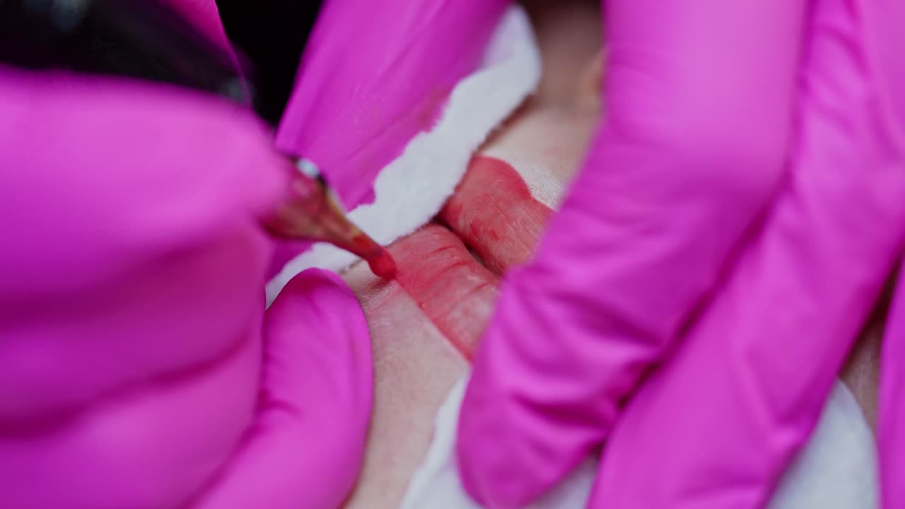 Tattoo machine doing makeup on woman's lips. Hands in pink gloves of a professional cosmetologist making permanent makeup on lips. Close-up.