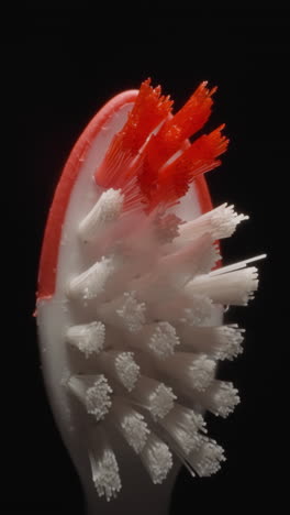 children toothbrush with hard bristles on black background. small red and white brush used for cleaning kids teeth. morning routine concept macro