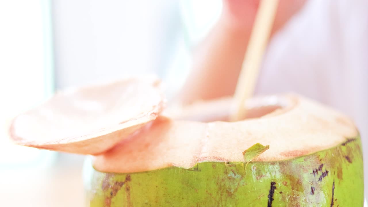 A person prepares a fresh coconut drink in bright, natural lighting, highlighting tropical refreshment in a relaxed setting