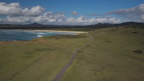 Back-view-of-isolated-person-walking-on-path-along-Look-at-me-now-Headland-with-Emerald-beach-in-background,-Australia