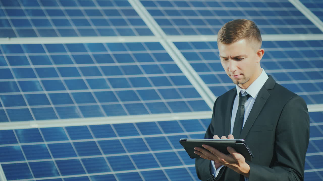젊은 사업가가 태양열 발전소 근처에서 태블릿을 사용합니다.