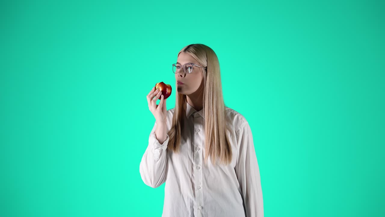 hermosa mujer joven disfruta de una manzana roja y jugosa, fondo turquesa, estudio