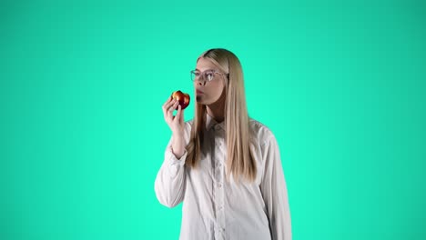 hermosa mujer joven disfruta de una manzana roja y jugosa, fondo turquesa, estudio