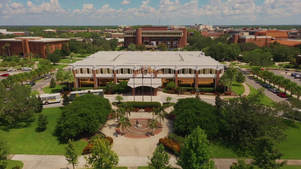 Veduta aerea della Millican Hall presso l'Università della Florida Centrale a Orlando, incorniciata da rigogliosi prati verdi, palme e il vasto campus dell'UCF sullo sfondo