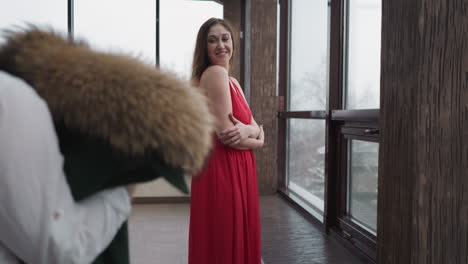 man carries coat for frozen woman on terrace. husband takes care of pretty wife wearing cocktail dress on cold day. happy relationship of couple