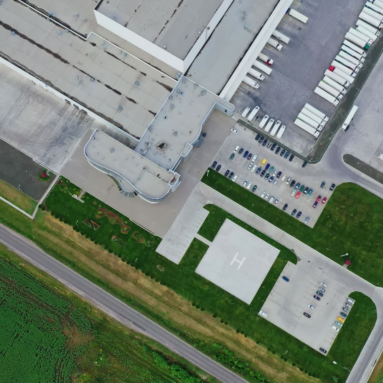 Factory on green field. View from above on industrial territory and many cars nearby. White trucks on the parking zone. Aerial view.