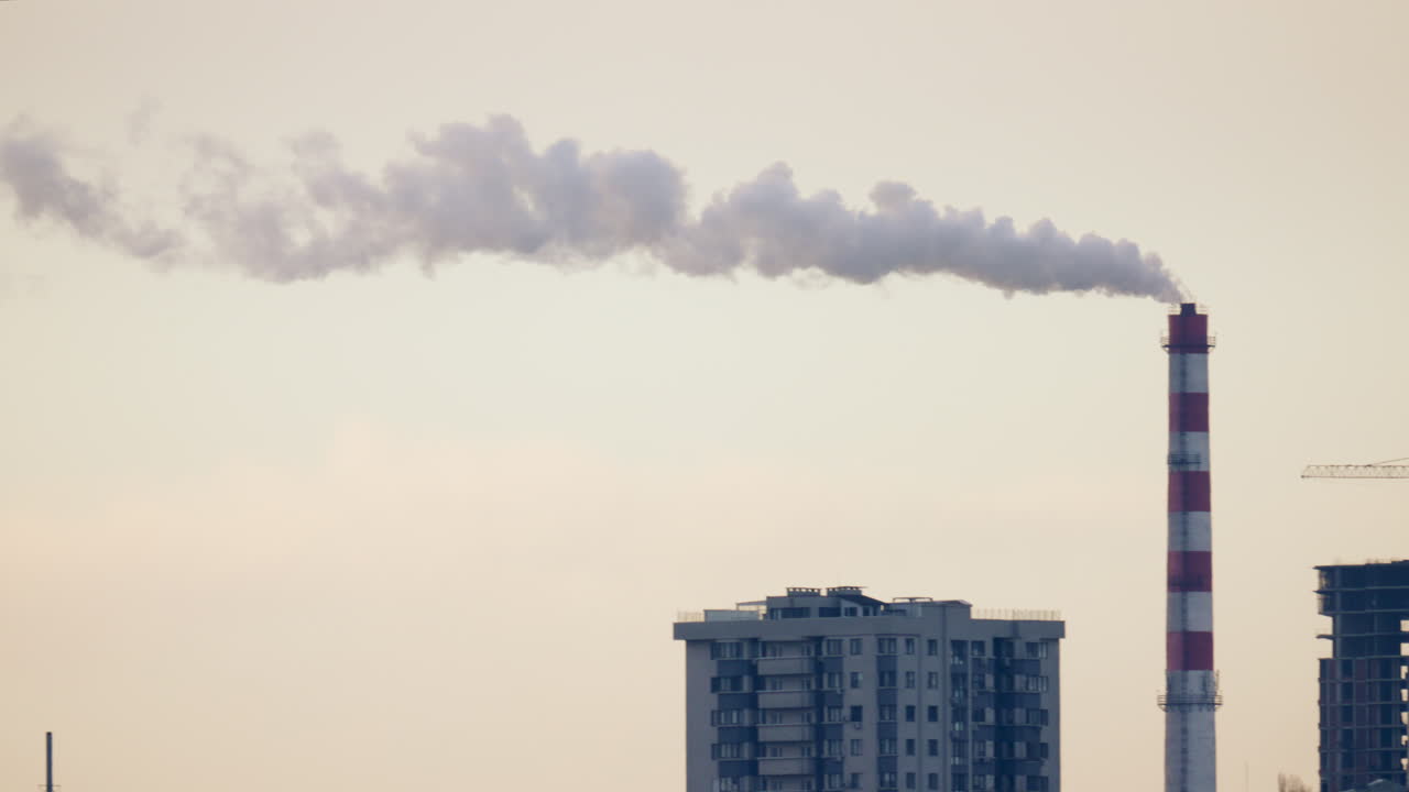 Urban skyline with residential buildings and an industrial chimney emitting smoke at sunset