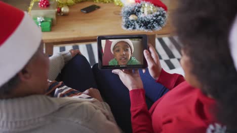 madre y hija afroamericanas usando una tableta para una videollamada de navidad con un niño en la pantalla