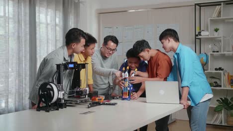 asian man with a laptop and 3d printing teaching the boys repairing a cyborg hand at school