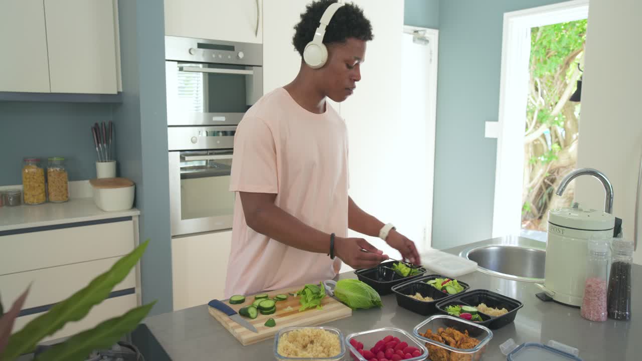 Adult male slicing cucumber on board at kitchen island, scooping rice into black meal boxes weekly