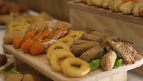 Mixed fried snacks including onion rings and shrimp on a wooden serving tray