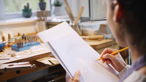 close up of female jeweller sketching out design for ring in studio