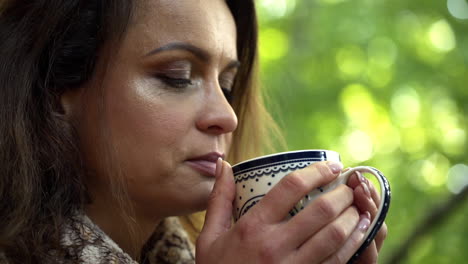 close up fhd shot of a brunette middle-aged woman tasting a cup of fresh hot tea in the morning and slowly opening her eyes