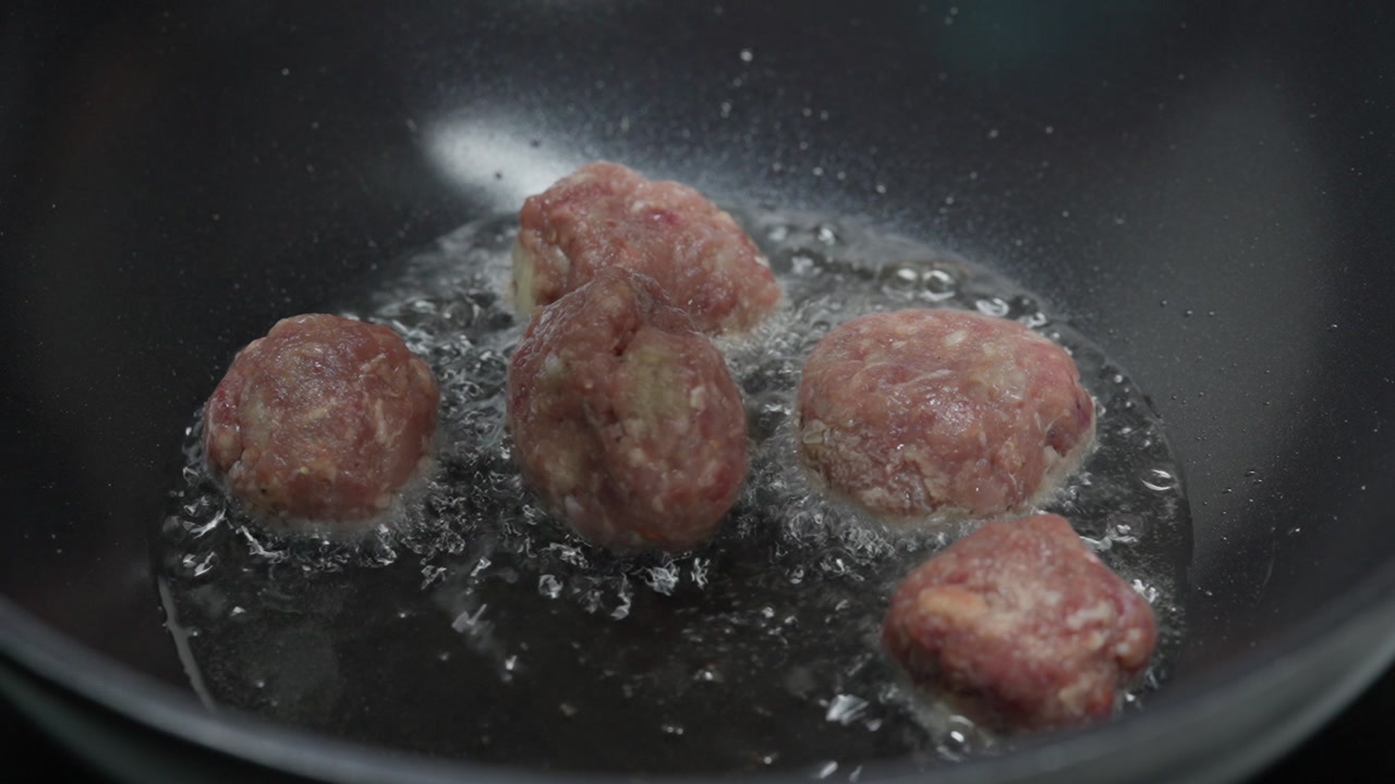 Close-up as raw meatball is placed into hot oil inside a cooking pan.