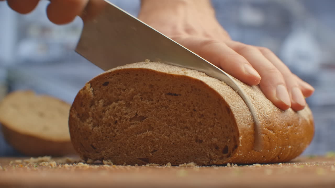 Cut bread with a knife on a wooden board closeup in the kitchen. shred