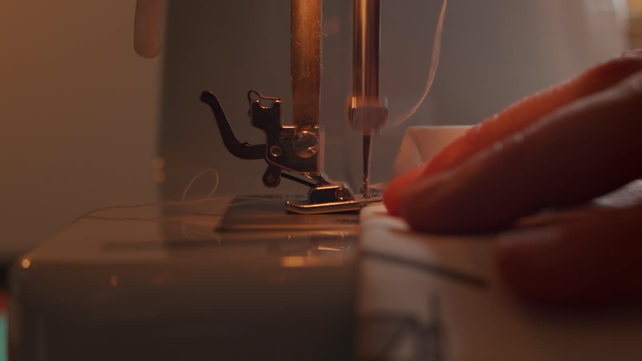 Side close view of slow motion needle of sewing machine and hands moving fabric as it is sewed