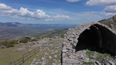 Seitlicher-Flug-Mit-Einer-Drohne-In-Der-Einsiedelei-Von-San-Pedro-Aus-Dem-14.-Jahrhundert-Mit-Ihrer-Besonderen-Gewölbten-Und-Halb-Zerstörten-Form,-Die-Sich-In-Einer-Faszinierenden-Umgebung-Befindet.-Es-Gibt-Einen-Blauen-Himmel-Mit-Wolken