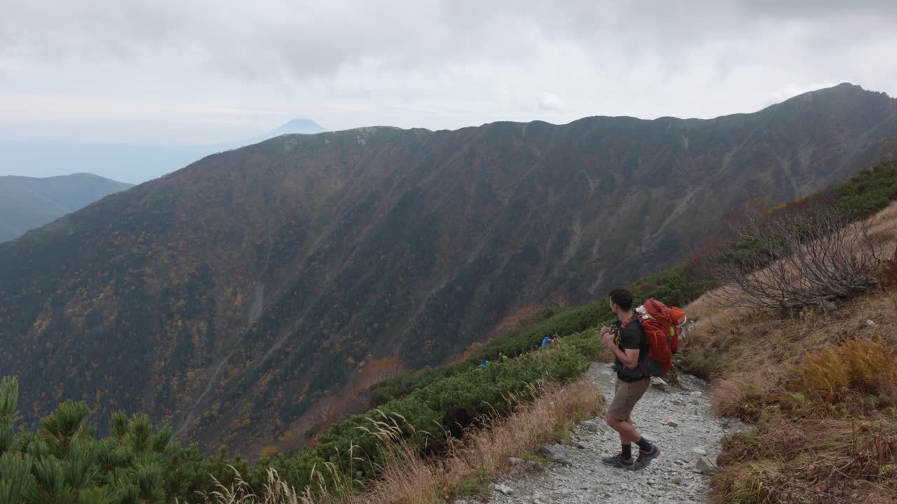 Young caucasian man with backpack hiking thorugh a mountain track with Mt. Fuji in the background in Mt. Kitadake, Japanese Alps