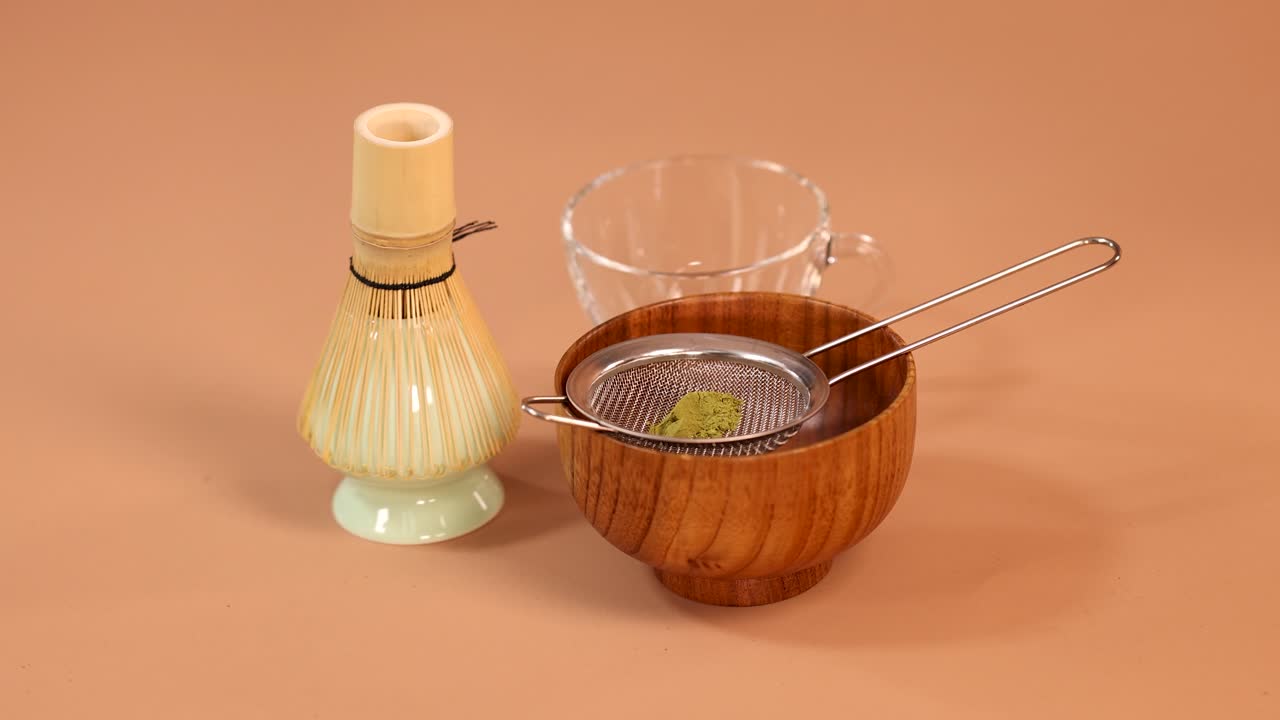 Hand sifts vibrant matcha powder through mesh strainer into wooden bowl, minimal studio lighting
