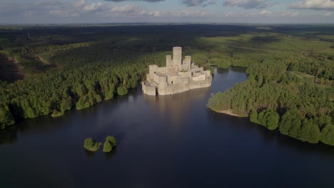 Toma-Aérea-Amplia-Del-Hermoso-Castillo-De-Stobnica,-Polonia---Una-Gran-Atracción-Turística-Construida-En-Una-Isla-Artificial-En-Un-Lago-En-Medio-De-Un-Bosque-Deshabitado