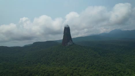 Flying backwards in a circular way over a palm plantation and having the Pico Cão Grande as a background with clouds covering the summit, São Tomé e Principe,Africa