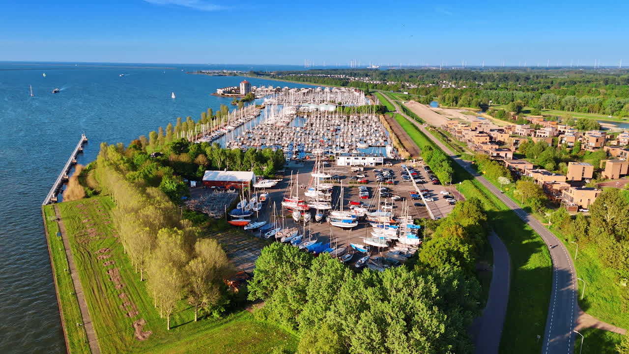 Green waterfront of lake Markermeer in Lelystad, the Netherlands. Drone footage approaching the yacht club with lots of vehicles.