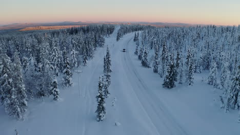 aerial view above snowy scandinavia landscape following vehicle on journey along long curved remote road through lapland woodland