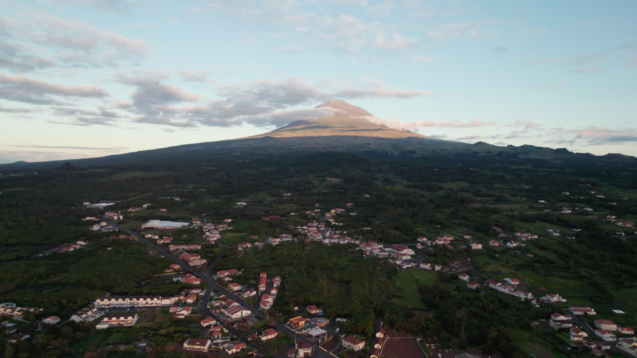 volar por encima de las mangueras en la ciudad, vista del majestuoso pico volcánico iluminado por la puesta del sol, ponta do pico