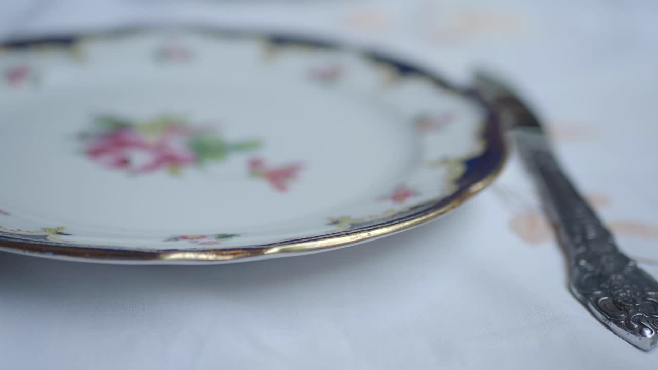 Primo piano di un piatto vintage con motivo floreale e posate su tovaglia bianca