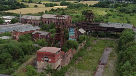 abandonada vieja mina de carbón cubierta de maleza edificios de museos industriales vista aérea tire hacia atrás lento