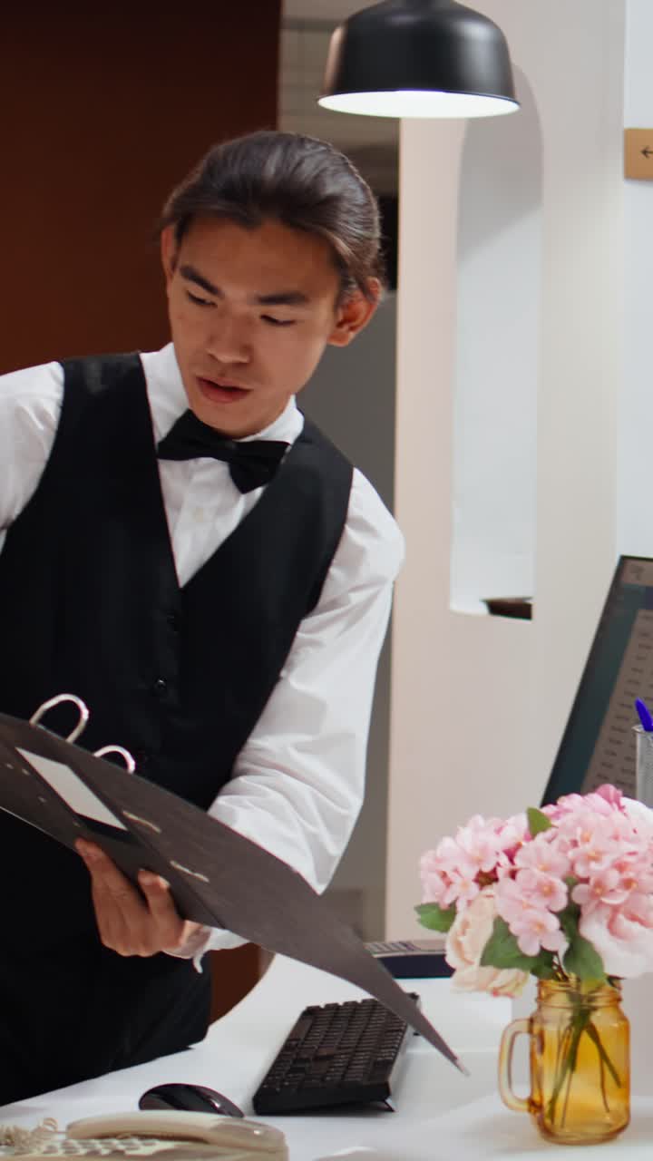 Video verticale: cliente asiatica chiede informazioni sull'alloggio al concierge dell'hotel