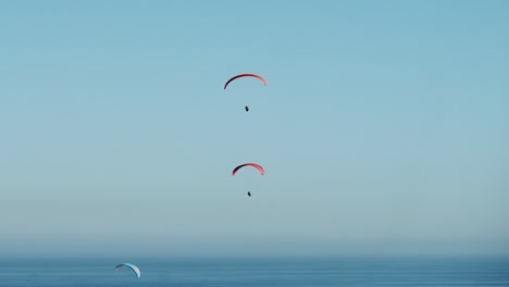 Parapentes-Volando-En-Cielos-Azules-Sobre-El-Océano,-Mañana-Soleada