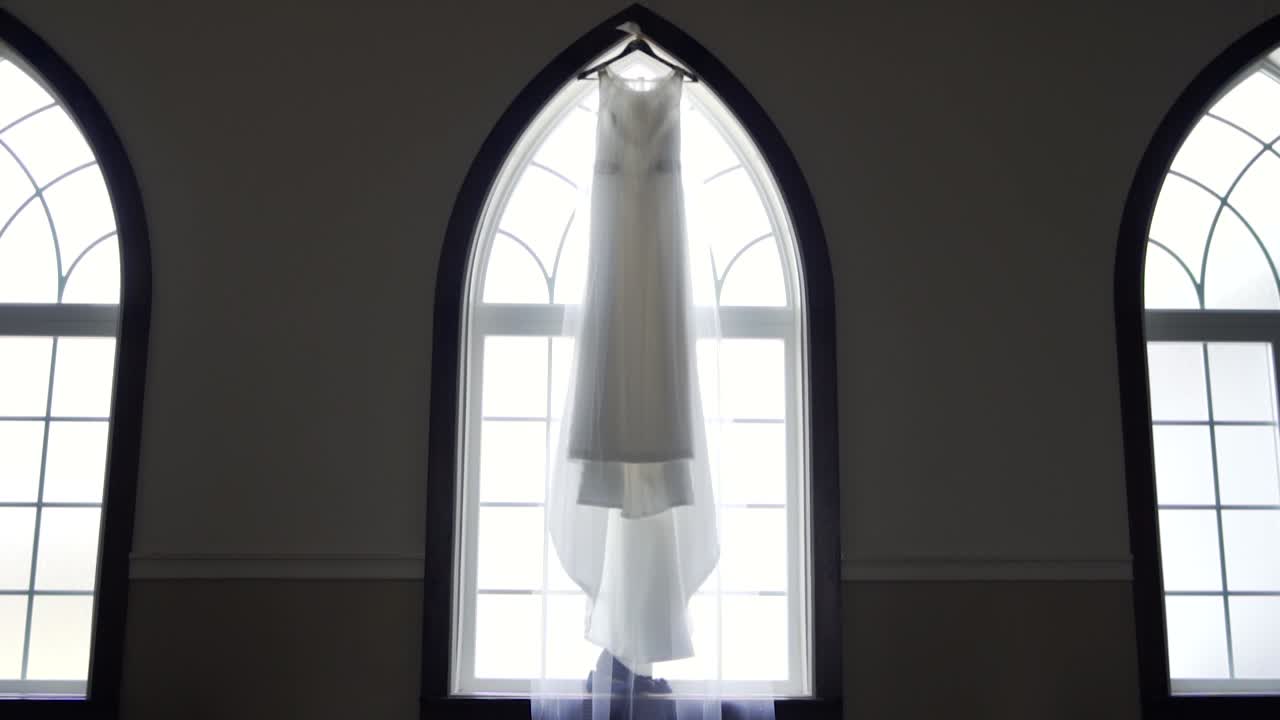 Ampia vista di un bellissimo abito da sposa appeso a un ampio davanzale in un vecchio edificio di chiesa - Carrellata lenta in avanti