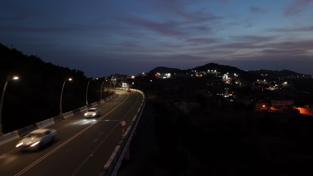 Aerial view of a black car driving on a illuminated elevation road in Saudi Arabia
