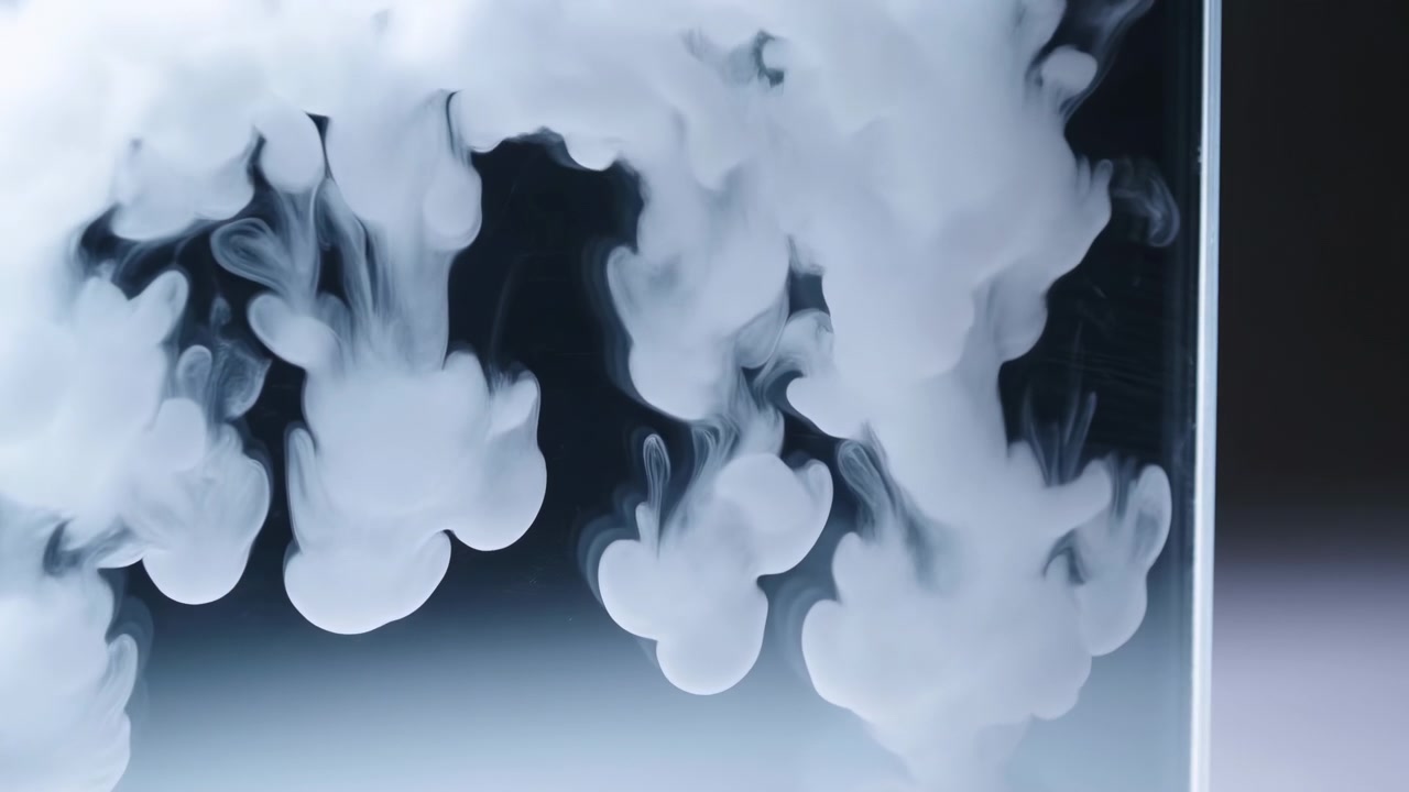Abstract white smoke-like plumes curl and spread near the top of a dark frame, creating soft contrast, fluid motion, and an atmospheric minimal texture