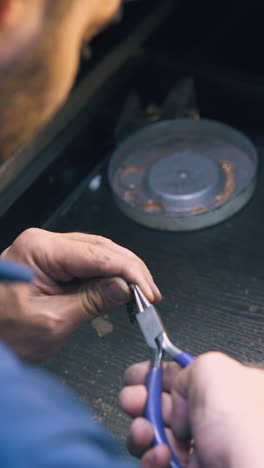cu: experienced goldsmith makes decorative metal chain with little links above table in jewelry workshop closeup