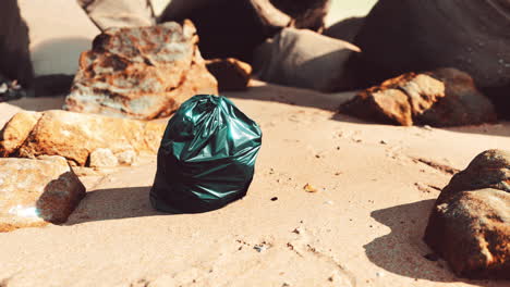 black plastic garbage bag full of trash on the beach