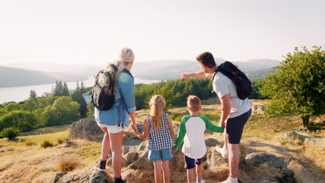 slow motion rear view shot of family standing at top of hill on hike through beautiful countryside in lake district uk