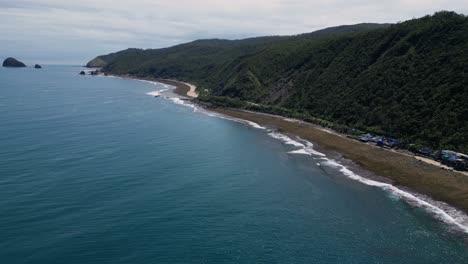 a wide drone shot captures the vast ocean waves crashing gently against the shore, with a majestic mountain rising in the distance.