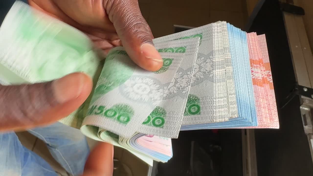 ภาพโคลสอัพมือที่ถือสกุลเงินไนจีเรียไนรา แสดงรายละเอียดของธนบัตร เงินสดในมือ ธุรกรรมทางการเงิน การชำระเงิน กิจกรรมทางธุรกิจ และการใช้เงินในชีวิตประจำวันในไนจีเรีย