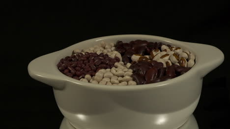 bowl of dry beans revolves isolated on black background, copy space